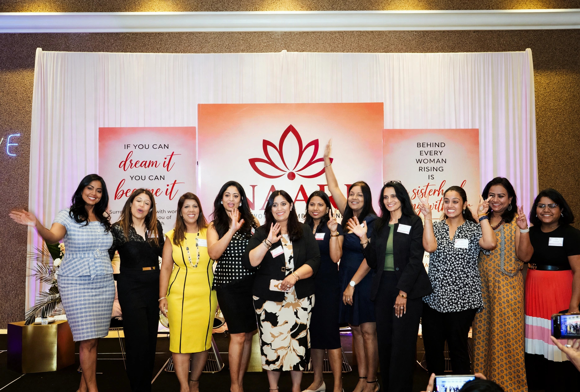 Ten women waving together at the NAARI backdrop